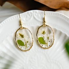 two white flowers are in a glass caballon with gold hoop earrings on a plate