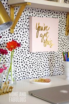 a white desk topped with vases filled with flowers next to a wall covered in polka dots