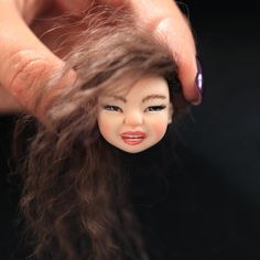 a close up of a doll being held by someone's hand with long hair