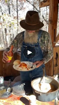 a man wearing overalls and a hat holding a plate with food in front of him