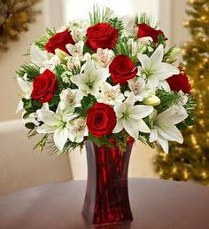 a red vase filled with white and red flowers next to a christmas card on a table