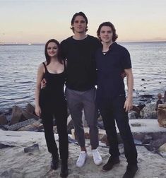 two men and a woman standing next to each other near the ocean