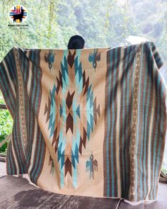 a blanket is draped on top of a wooden table in front of some trees and bushes