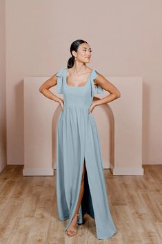 a woman in a grey dress standing on a wooden floor with her hands on her hips