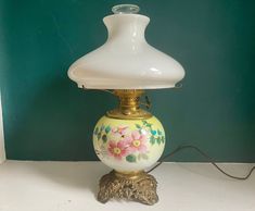 a white lamp sitting on top of a table next to a green wall with flowers painted on it