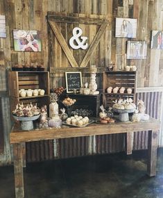 a table topped with lots of cakes and cupcakes next to a wooden wall