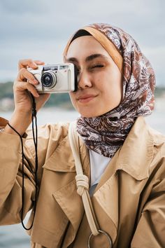 a woman taking a photo with her camera on the beach while wearing a headscarf