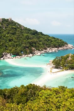 an island with white sand and blue water surrounded by green trees in the foreground