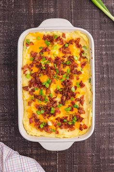 a casserole dish with bacon, cheese and green onions in it on a wooden table