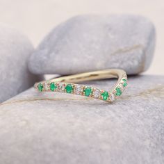 a diamond and emerald band ring sitting on top of a rock next to some rocks