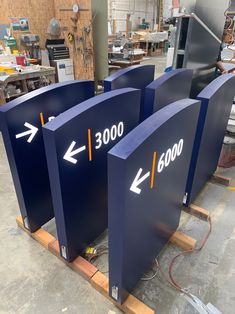 three large blue signs with arrows pointing in different directions on wooden pallets inside a building