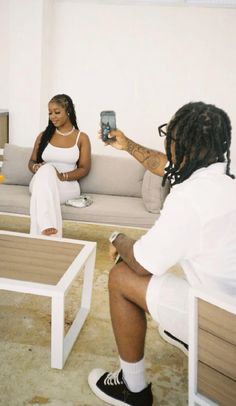 a woman sitting on a couch taking a photo with her cell phone while another person sits in the background