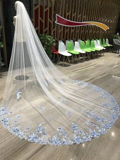 a wedding veil with blue flowers on the bottom is sitting in front of some chairs