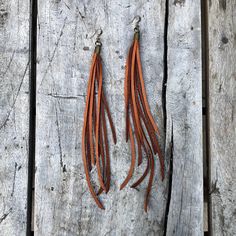 two pairs of orange leather tassels hanging from hooks on wooden planked surface