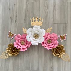 paper flowers with gold leaves and a crown on top are laying on a wood floor