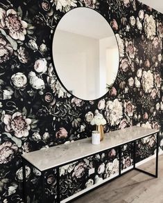 a black and white floral wallpaper with a round mirror on the end table in front of it