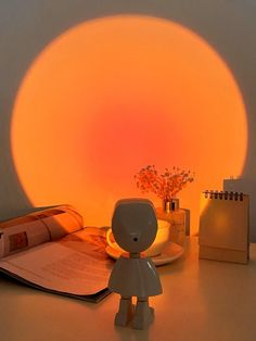 a small toy standing in front of an open book on a table next to a lamp