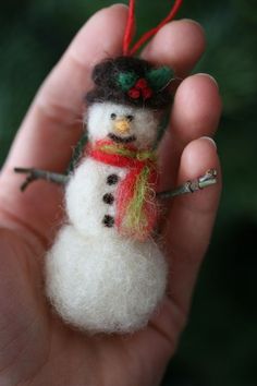 a small snowman ornament is held in someone's hand with a needle