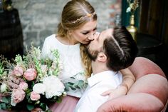 a man kissing a woman on the cheek with flowers in front of her and an old brick wall behind them