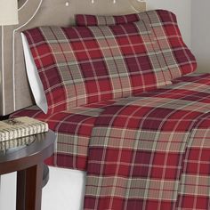 a bed with plaid sheets and pillows on top of it next to a night stand