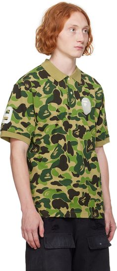 Cotton piqué polo. Camouflage logo pattern printed throughout. · Rib knit spread collar and cuffs · Two-button placket · Logo graphic embroidered at front · Vented side seams · Text applique at sleeves Supplier color: Green Collared Polo Shirt With Graphic Print For Streetwear, Graphic Print Collared Polo Shirt For Streetwear, Collared Polo Shirt With Logo For Streetwear, Streetwear Collared Polo Shirt With Logo Print, Green Cotton Polo Shirt For Streetwear, Casual Polo Shirt With Embroidered Logo For Streetwear, Casual Polo Shirt With Logo Patch, Designer Collared Polo Shirt With Logo, Green Collared Polo Shirt With Button Closure