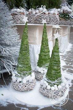 three small christmas trees sitting on top of snow covered ground next to baskets filled with balls