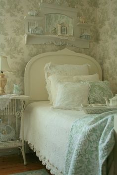 a white bed sitting in a bedroom next to a wallpaper covered with green and white flowers