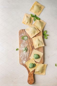 ravioli with pesto and parmesan cheese on a wooden cutting board next to basil leaves