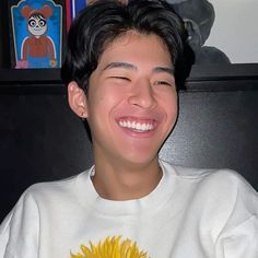 a young man smiling and wearing a white shirt with a sunflower on it's chest