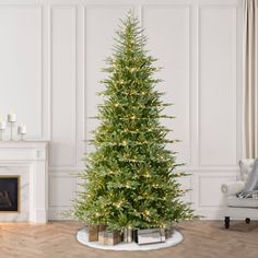 a christmas tree in a living room with white walls and wood flooring, lit by lights