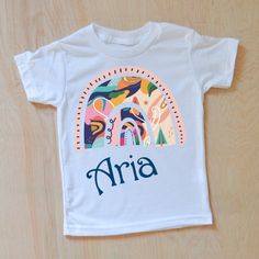 Personalized kids t-shirts with a colorful rainbow. The perfect gift for little ones. Made in America. This personalized kids t-shirt is part of our Be Mine Collection. Playful Colorful Crew Neck T-shirt, White Cotton T-shirt With Rainbow Print, Multicolor Graphic Tee T-shirt As Gift, Cute Multicolor T-shirt With Rainbow Print, Playful Multicolor Rainbow Print T-shirt, Cute Multicolor Rainbow Print T-shirt, Playful Rainbow Print Top, Playful Rainbow Graphic Print T-shirt, Colorful Playful Short Sleeve T-shirt