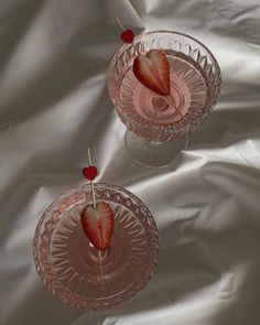 two glasses with strawberries in them on a white cloth