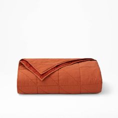 an orange quilted blanket folded on top of a white surface with the cover pulled down