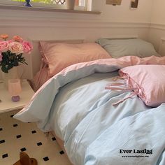 an unmade bed with pink and blue comforters in a white room next to a window