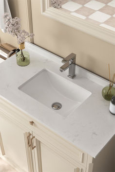 a white bathroom sink sitting on top of a counter next to a mirror and vase with flowers