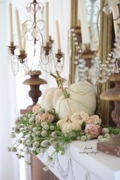 white pumpkins and flowers sit on a mantle in front of a chandelier