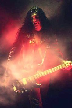 a man with long hair holding a bass in front of a black and white background