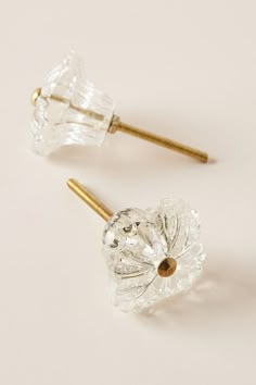 two clear glass knobs with gold tips on white surface, one is closed and the other has an ear pin