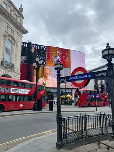 a red double decker bus driving down a street next to a tall building with advertisements on it