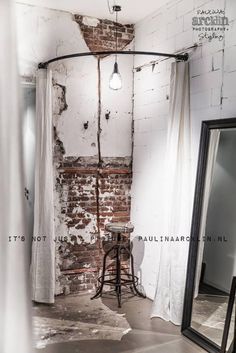 an old brick wall with exposed pipes and a round table in the corner next to a mirror