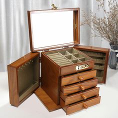 an open wooden jewelry box sitting on top of a white table next to a vase