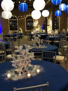 tables with blue linens and white paper snowflakes are set up for an event