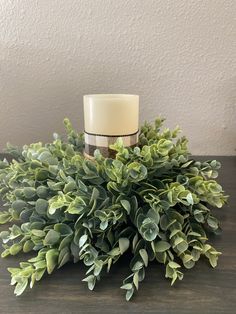 a white candle sitting on top of a wooden table next to some green plants and leaves