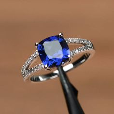 an engagement ring with a blue stone surrounded by white diamonds on a black stand in front of a brown background