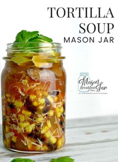 a mason jar filled with corn, black olives and basil leaves on top of a wooden table