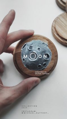 a hand holding a wooden button with the word moon printed on it in black and white