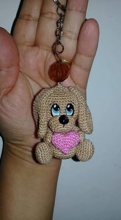 a hand holding a small key chain with a dog on it's chest and a heart in its mouth