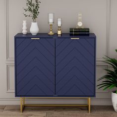 a blue cabinet with gold handles and two vases on top, next to a potted plant