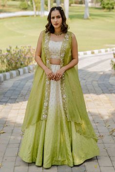 a woman in a green and white lehenga standing on a brick walkway with trees in the background