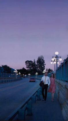 a man and woman are walking down the sidewalk at dusk with their arms around each other